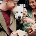 Smiling couple shares a moment with their Labrador retriever during an outdoor picnic.