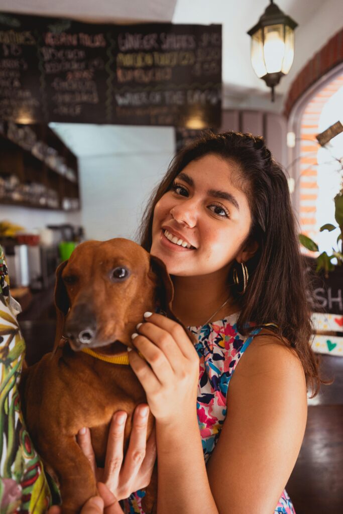 A cheerful young woman indoors holding her Dachshund pet, both smiling at the camera.